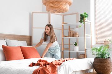 Pretty young woman making bed in modern bedroom