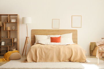 Interior of cozy bedroom with soft blankets on bed, lamp and shelf unit