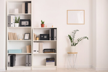 Modern safes, houseplants and office folders on shelving unit near white wall