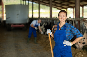Portrait of woman working on livestock farm posing in outdoor cowshed near stall with herd of cows