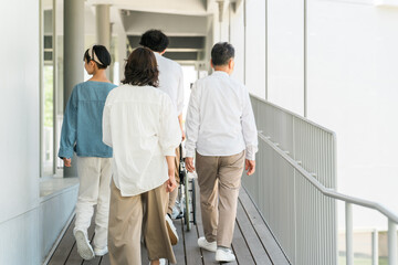 Fototapeta premium 病院・介護施設・老人ホームの廊下を車椅子を押しながら歩く三世代家族 