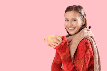 Young woman in warm sweater with cup of tea on pink background