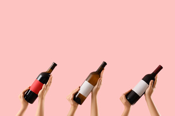 Female hands holding bottles of wine on pink background