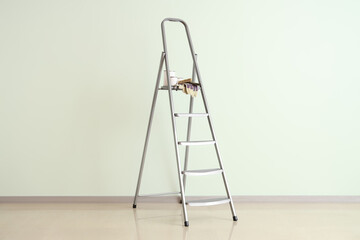 Stepladder with cans of paint and brushes near green wall