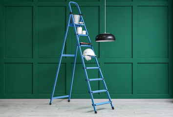 Stepladder with cans of paint and brushes near green wall