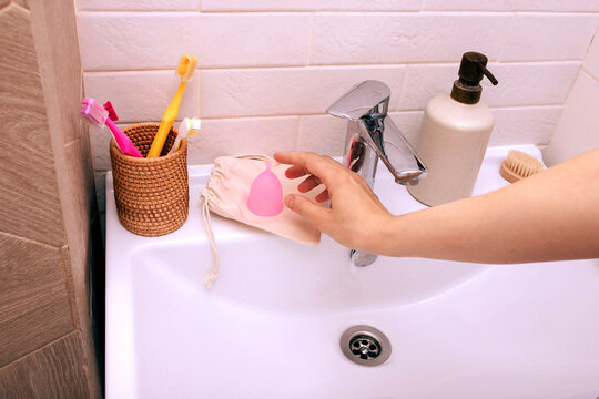 A woman's hand with pink menstrual cup against bathroom background.