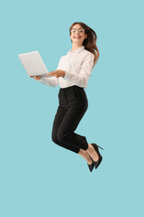 Young businesswoman with laptop jumping on blue background