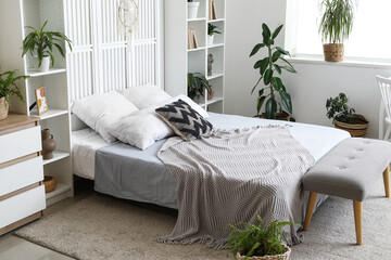 Cozy bed, shelving units and houseplants in interior of bedroom