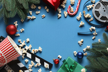 Frame made of bucket of popcorn, film reel, movie clapper and Christmas decor on blue background