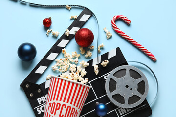 Bucket of popcorn, film reel, movie clapper and Christmas decor on blue background