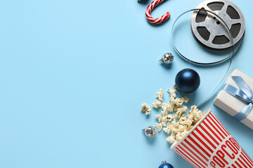 Bucket of popcorn, film reel, gift box and Christmas decor on blue background