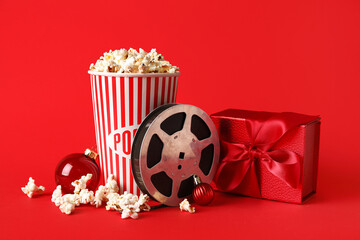 Bucket of popcorn, film reel and Christmas decor on red background