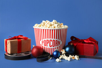 Bucket of popcorn, film reel, gift boxes and Christmas balls on blue background