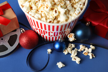 Bucket of popcorn, film reel, gift boxes and Christmas balls on blue background, closeup