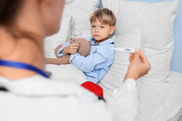 Little boy ill with chickenpox and doctor holding thermometer in bedroom