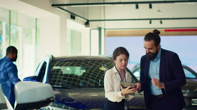 Overjoyed customer dancing around car showroom after picking purchase option, satisfied with choice. Cheerful man receiving vehicle keys from saleswoman, celebrating, camera A
