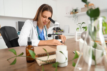 Female homeopathic doctor looking through microscope at table in office