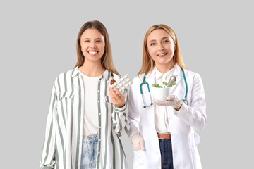 Female homeopathic doctor and young woman with remedy on light background