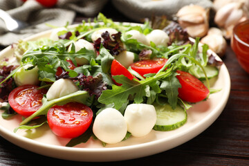 Tasty salad with arugula, lettuce, mozzarella cheese and vegetables on wooden table, closeup