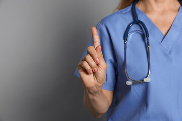 Doctor pointing at something on gray background, closeup. Space for text