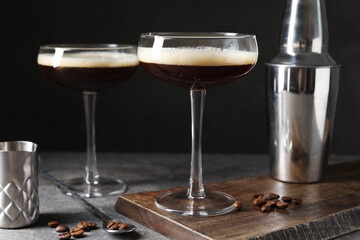 Glasses of delicious espresso martini, shaker and coffee beans on dark textured table, closeup
