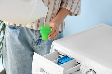 Woman pouring laundry detergent near washing machine in room, closeup