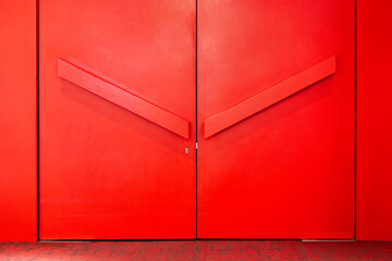 Minimalist bright red double doors with geometric V-shaped design elements. Modern architectural detail against vibrant monochromatic background.