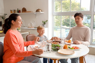 Little boy with his parents praying before eating Fajita at table in kitchen