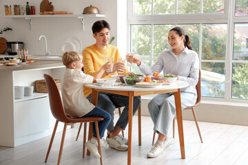 Little boy and his parents with glasses of water eating Fajita at table in kitchen