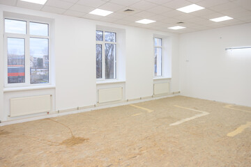 Spacious school room under renovation with large windows and unfinished floor