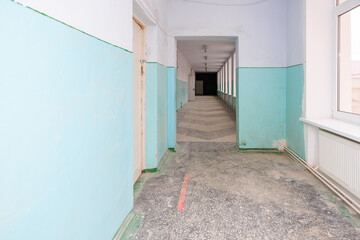 Long corridor in an old school with worn flooring and faded walls, awaiting renovation