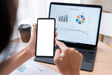 Businesswoman analyzing financial charts on laptop and holding smartphone with white screen