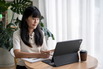 Young asian woman working from home using digital tablet and taking notes