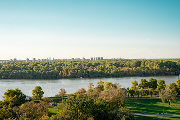 Fototapeta premium beautiful view of the city landscape during sunset, The Danube River meanders through a landscape where tall trees meet rolling hills in the background. The sky is partly cloudy, and the hills create 