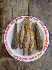 Delicious fried salted fish or ikan pindang in a plate on wooden table.