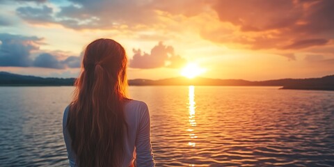 Fototapeta premium Silhouette of woman watching golden sunset over calm water