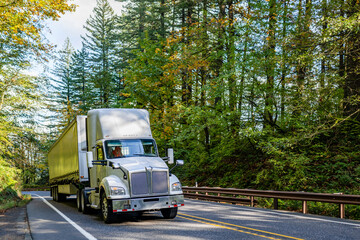 Big rig day cab white semi truck with huge roof spoiler transporting cargo in conestoga flat bed...