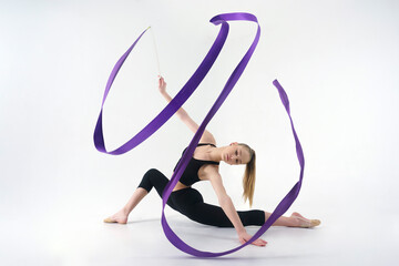 young gymnast in a photo studio shows the elements of exercises with a ribbon, doing stretching and rotating it