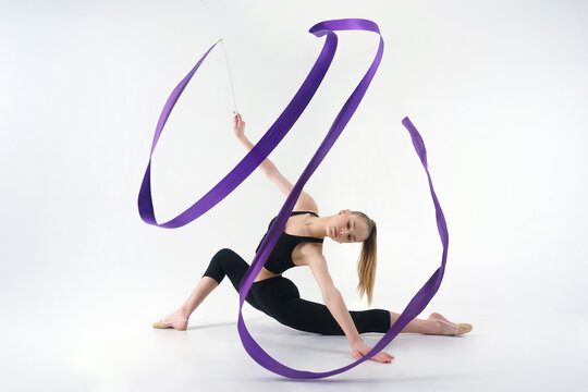 young gymnast in a photo studio shows the elements of exercises with a ribbon, doing stretching and rotating it