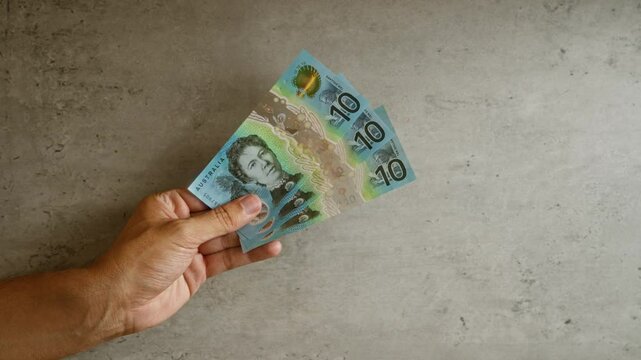 Hand holding australian dollars against a concrete backdrop showcasing three ten-dollar notes.