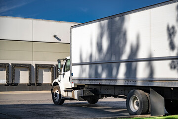 Day cab middle duty white rig semi truck with long box trailer standing on the warehouse industrial...