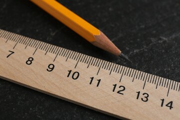 Wooden ruler and pencil on black table, closeup