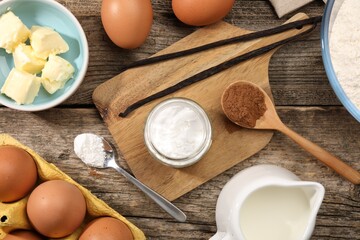 Baking powder in bowl surrounded by other products on wooden table, flat lay