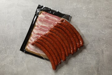 Packs of dry smoked sausages and sliced bacon on grey table, top view