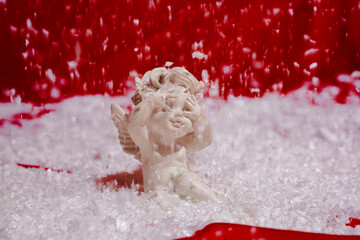 Valentine's Day. Statuette of an angel with snow. Angel-cupid at red background. The concept of...