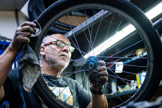 Concentrated mechanic man with some eyeglasses fixing bike wheel on work desk in bikeshop - Powered by Adobe