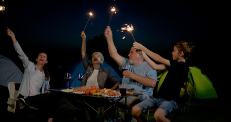 family with grandparents having fun and playing fire sparkle while camping in the outdoors  with smiles, laughter, and joy, celebrating together