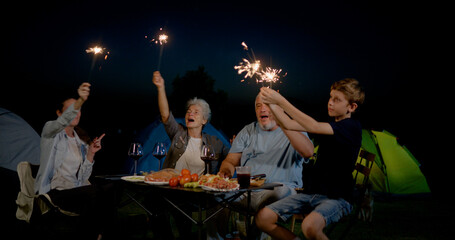family with grandparents having fun and playing fire sparkle while camping in the outdoors  with...