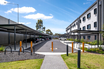 Fototapeta premium Modern apartment complex building, car park with covered parking bays or carports, and pedestrian walkways in a residential development. An organized parking infrastructure with bollards.