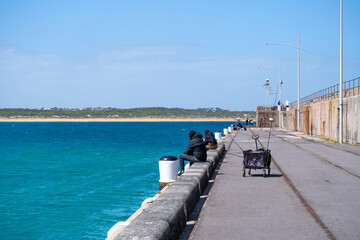 Obraz premium A scenic view along the breakwater at Warrnambool, Australia, with people enjoying the coastal environment. An attraction, fishing and sightseeing spot with deep blue ocean view.